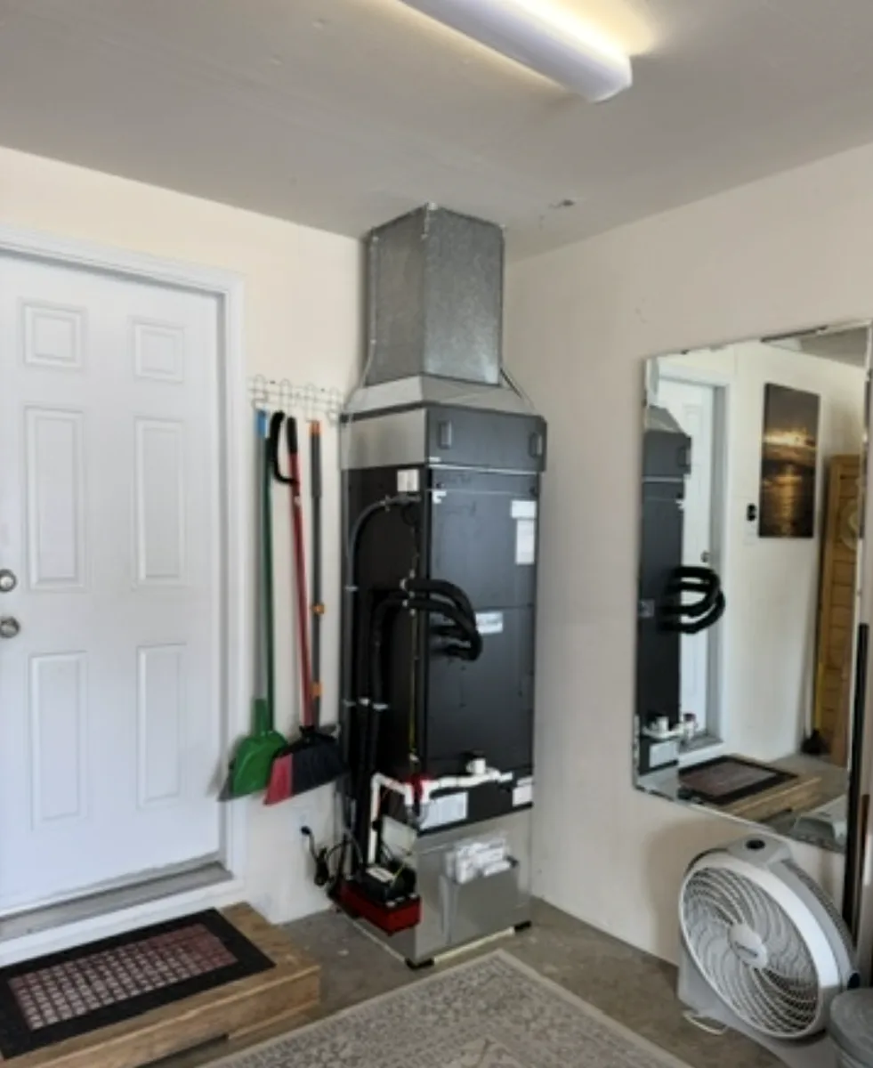 Heat pump air handler installed in a garage with the refrigerant line set and condensate drain routed to the front.