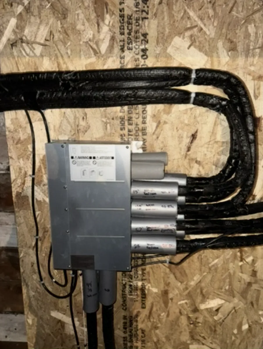 Branch box for a multi-zone heat pump system, each line set labelled by hand with the room it serves and its run length.